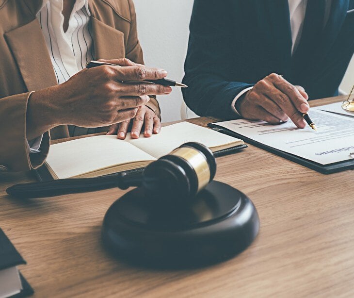 Image of two people talking and looking at paperwork. A gavel is also pictured. 