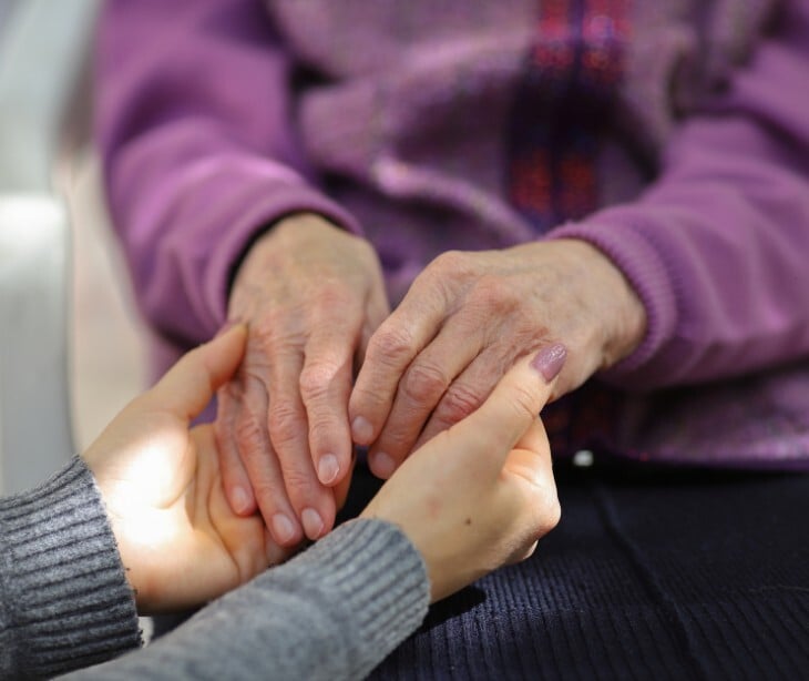 Image of an individual holding hands with an elderly individual. 