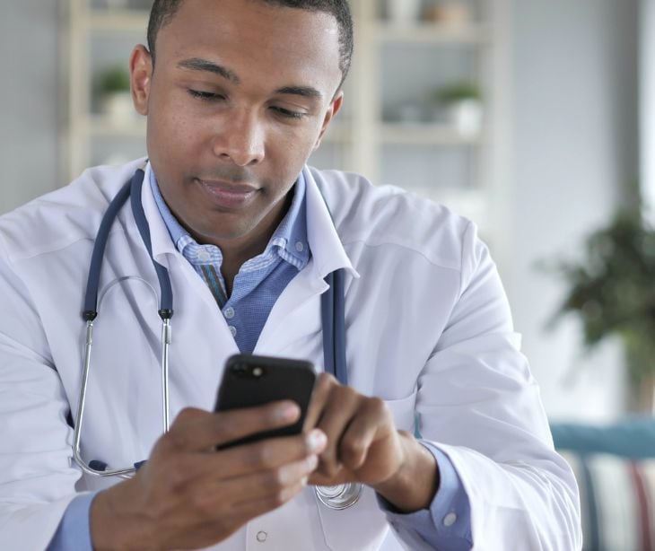 provider in white coat using cellphone for post Can healthcare providers use personal devices for patient communication?