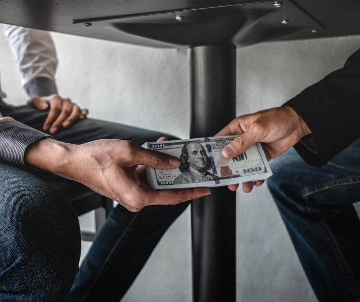 Image of someone handing someone else money under a table. 