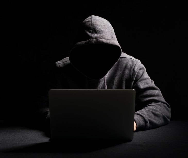 Image of an individual hooded on a laptop. 