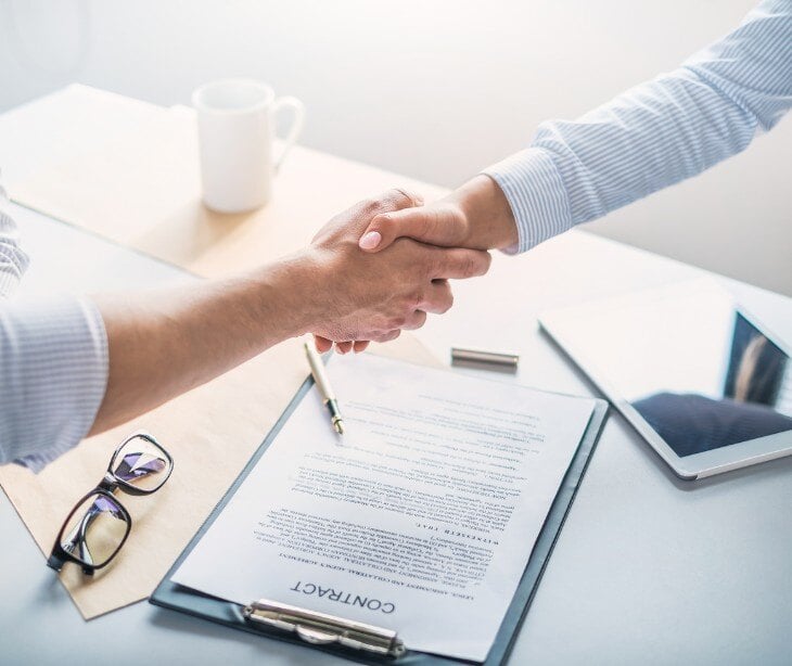 Image of two people shaking hands over a piece of paper. 