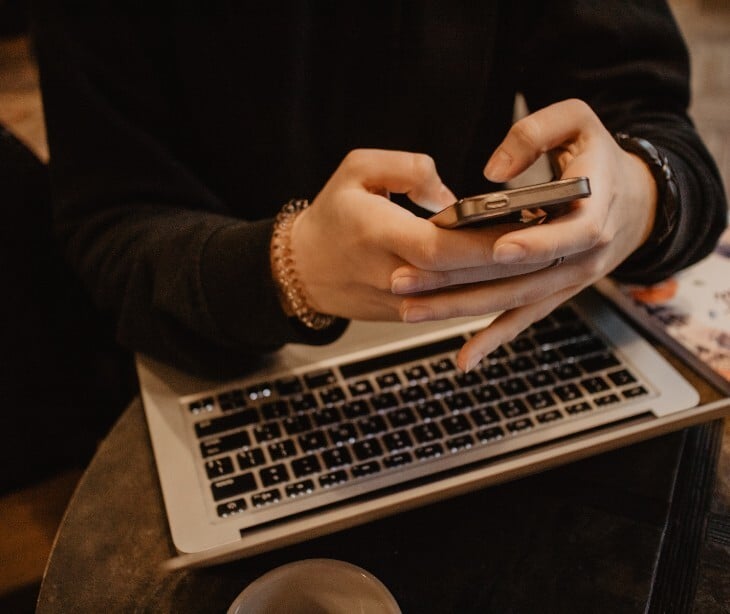 Image of someone sending a text on their phone with a computer open. 