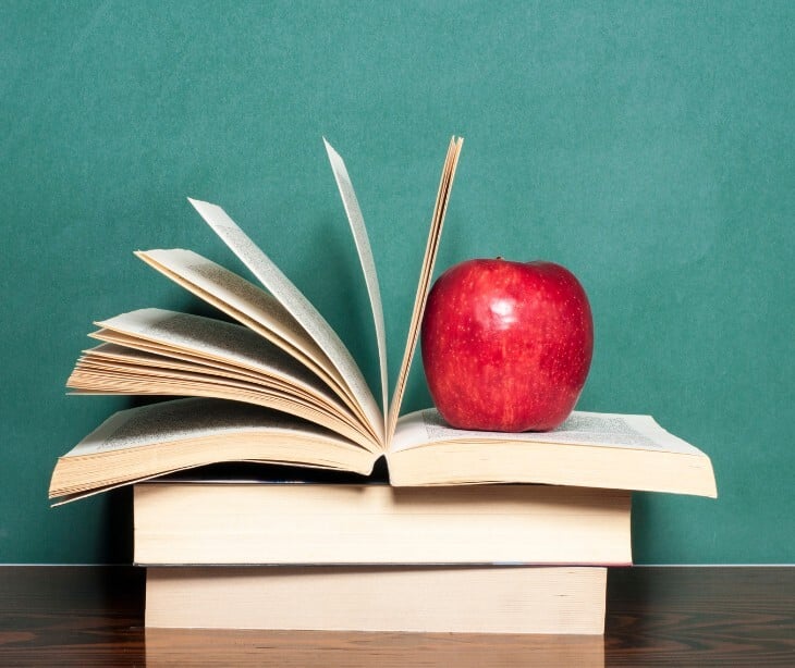 Image of a stack of books, one with an apple on it. 