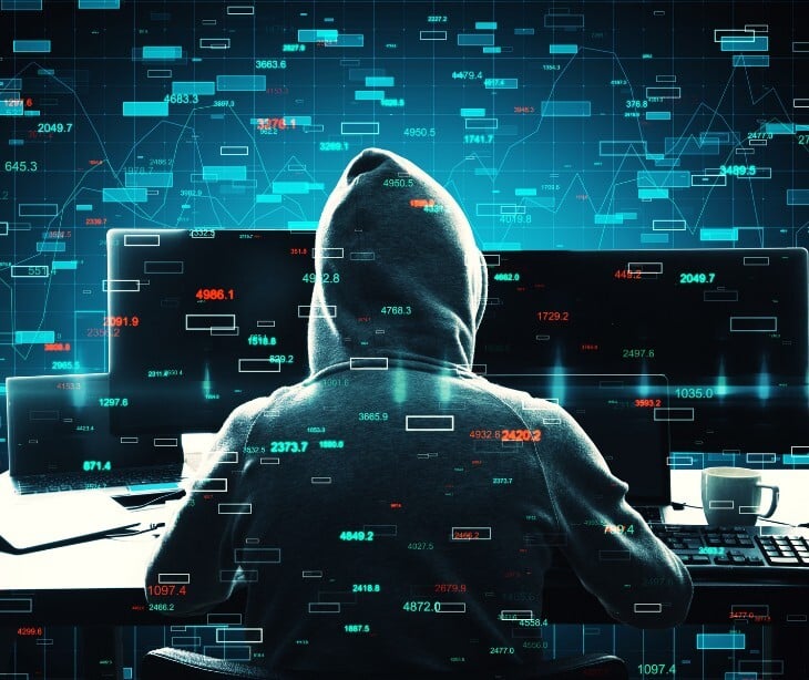 Image of a hooded figure sitting behind a computer. 