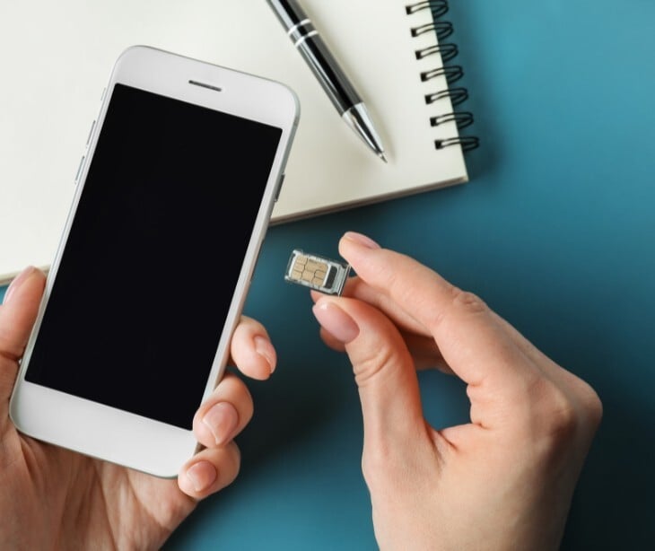 Image of someone holding their phone and a SIM card. 