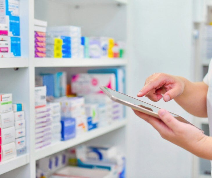 Image of someone looking at medicine in a pharmacy, holding a tablet. 