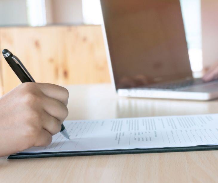 hand filling out form with laptop in background