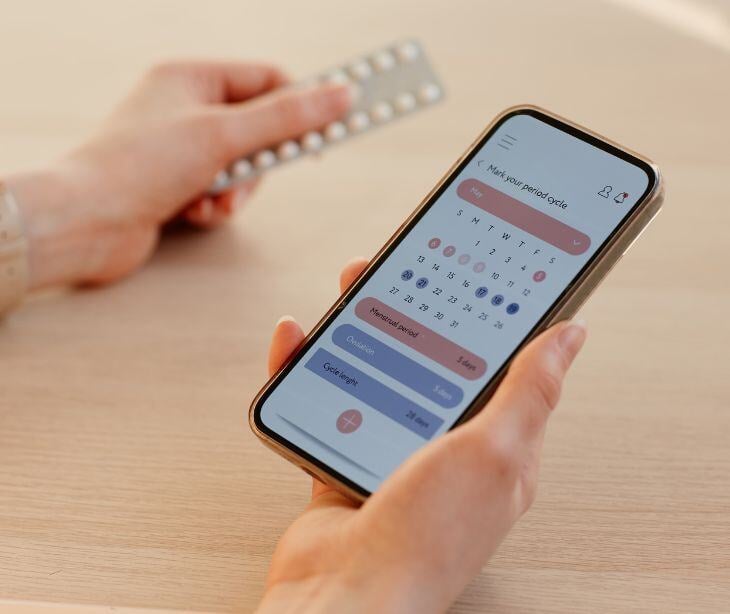 woman holding smartphone with calendar app holding pill packet