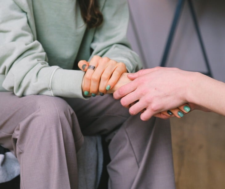 Image of an individual comforting another individual by holding their hand. 