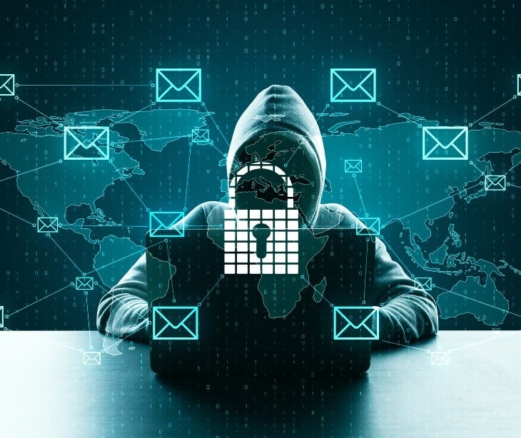 Image of a hooded figure in a computer with email icons surrounding them. 