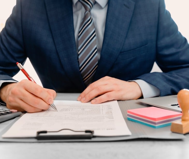 Image of someone in a suit signing a document. 