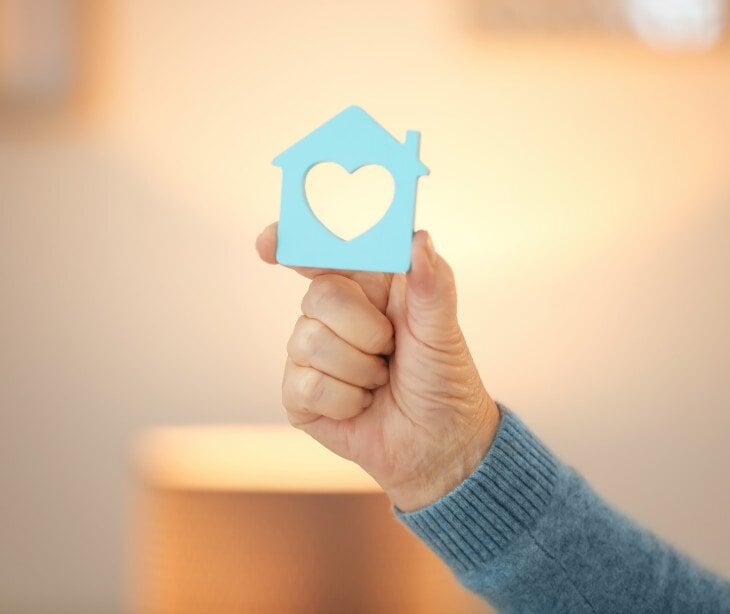 Image of someone holding a paper cut out of a blue home, with a heart inside.